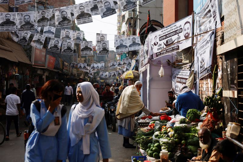 FILE PHOTO: Posters of an election candidate hang on the street as people buy vegetables from a street vendor ahead of the general election in Dhaka