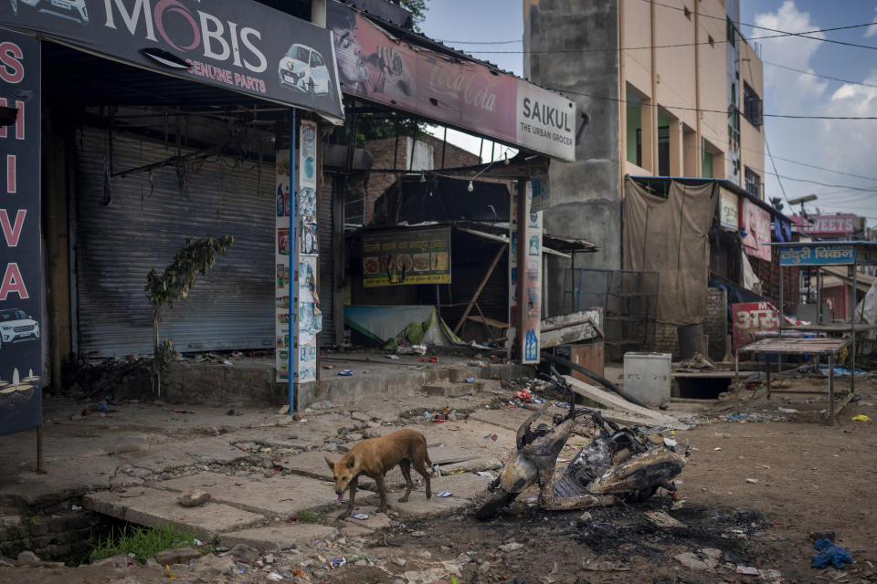 A stray dog stands next to a burnt scooter and partially burnt shops in Sohna near Nuh in Haryana state, India, Tuesday, Aug., 1, 2023. Deadly clashes between Hindus and Muslims began in the area Monday afternoon during a religious procession by a Hindu nationalist group forcing Indian authorities to impose a curfew and suspend Internet services. (AP Photo/Altaf Qadri)