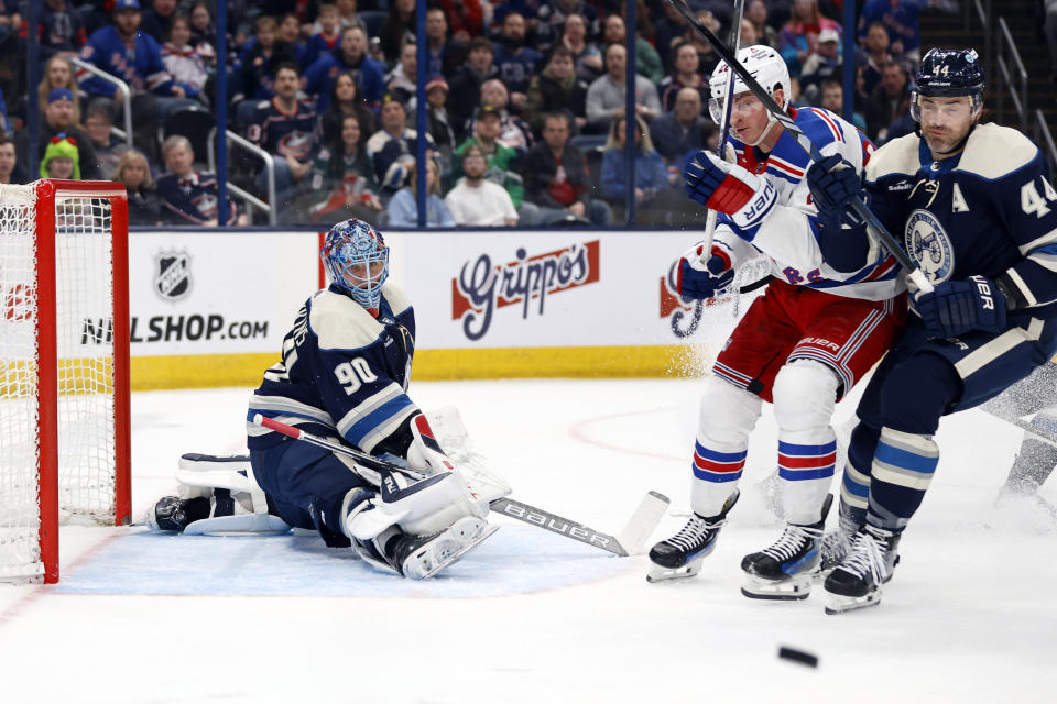 Columbus Blue Jackets goalie Elvis Merzlikins, left, makes a stop in front of New York Rangers forward Jimmy Vesey, center, and Blue Jackets defenseman Erik Gudbranson, right, during the first period of an NHL hockey game in Columbus, Ohio, Sunday, Feb. 25, 2024. (AP Photo/Paul Vernon)