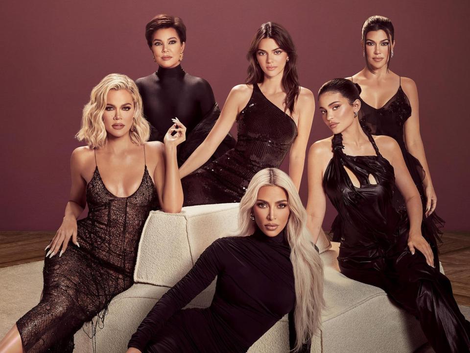 A promotional shot of Kris Jenner, Kourtney Kardashian, Kim Kardashian, Khloé Kardashian, Kendall Jenner, and Kylie Jenner sitting around a sofa in a room with a burgundy colored wall.