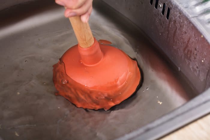 sink plunger being used to unclog kitchen sink drain