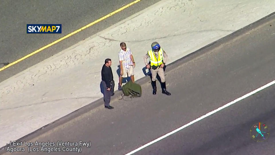 This photo taken from video provided by KABC-TV shows a man, center, believed to be the pilot of a vintage North American AT-6 airplane that crashed on U.S. 101 in Agoura Hills, Calif., Tuesday, Oct. 23, 2018. The pilot escaped uninjured and no one on the ground was hurt. The crash snarled traffic about 30 miles (50 kilometers) west of downtown Los Angeles. (KABC-TV via AP)