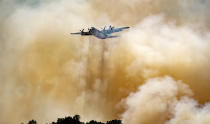 A firefighting aircraft flies through smoke after dropping fire retardant on a hillside in an attempt to box in flames from a wildfire locally called the Sand Fire in Rumsey, Calif., Sunday, June 9, 2019. (AP Photo/Josh Edelson)