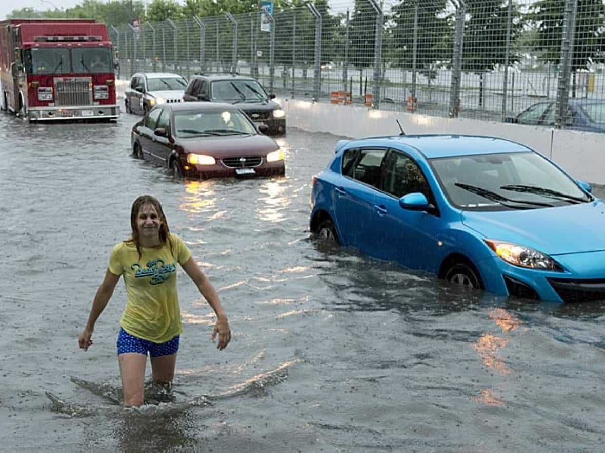 A woman wading through floodwaters during a storm in Toronto in 2013. The auditor general says the province must do more to prevent urban flooding. (Frank Gunn/The Canadian Press - image credit)