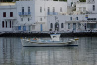 In this Tuesday, June 9, 2020, photo, a fishing boat is anchored in front of the main walkway on the Greek island of Mykonos, Greece. Business owners and locals officials on the Greek holiday island of Mykonos, a popular vacation spot for celebrities, club-goers, and high rollers, say they are keen to reopen for business despite the risks of COVID-19 posed by international travel. Greece will officially launch its tourism season Monday, June 15, 2020 after keeping the country's infection rate low. (AP Photo/Derek Gatopoulos)