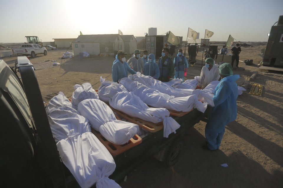 Members of the Shiite Imam Ali brigades militia load bodies of a coronavirus victims during a funeral at Wadi al-Salam cemetery near Najaf, Iraq, Monday, July 20, 2020. A special burial ground near the Wadi al-Salam cemetery has been created specifically for COVID-19 victims since rejections of such burials have continued in Baghdad cemeteries and elsewhere in Iraq. (AP Photo/Anmar Khalil)
