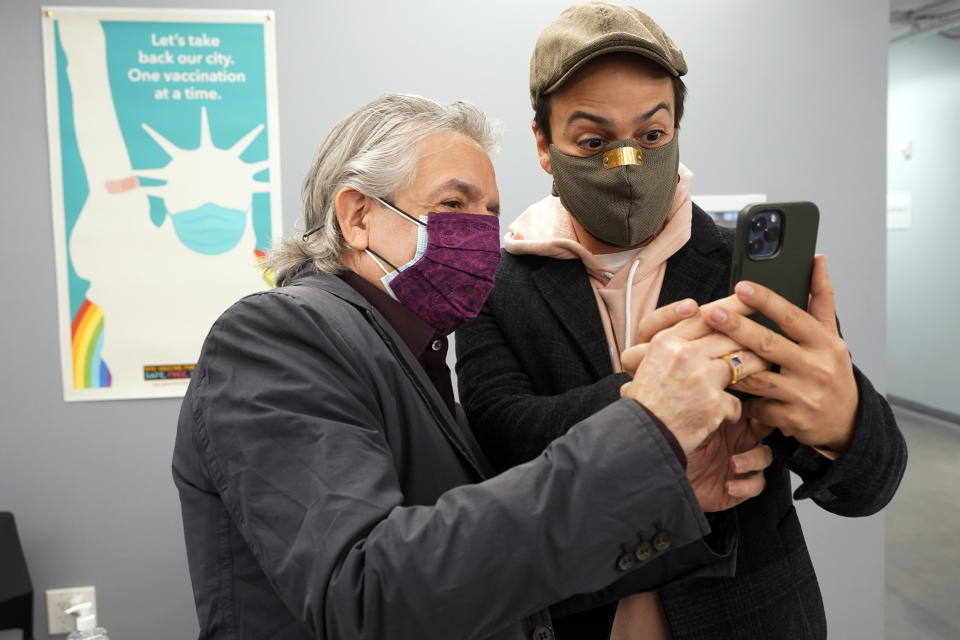 Actor Lin-Manuel Miranda, right, and his father, Luis A. Miranda, Jr., look at a mobile phone before they tour the grand opening of a Broadway COVID-19 vaccination site intended to jump-start the city's entertainment industry, in New York, Monday, April 12, 2021. (AP Photo/Richard Drew, Pool)