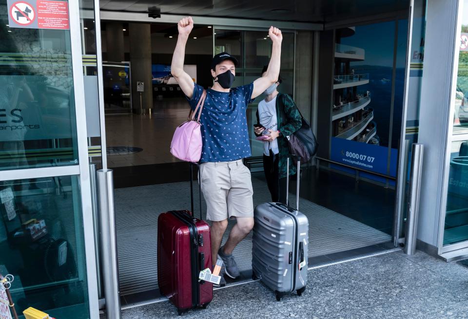 A traveller, mask-clad due to the COVID-19 coronavirus pandemic, arriving on one of the first flights from Britain gestures as he walks with luggage out of the terminal at Cyprus' Larnaca International Airport on August 1, 2020. - British visitors returning to Cyprus are set to give the holiday island's tourism sector a welcome boost after a battering by the pandemic, but some locals are sceptical about how big the gains will be. (Photo by Iakovos Hatzistavrou / AFP) (Photo by IAKOVOS HATZISTAVROU/AFP via Getty Images)