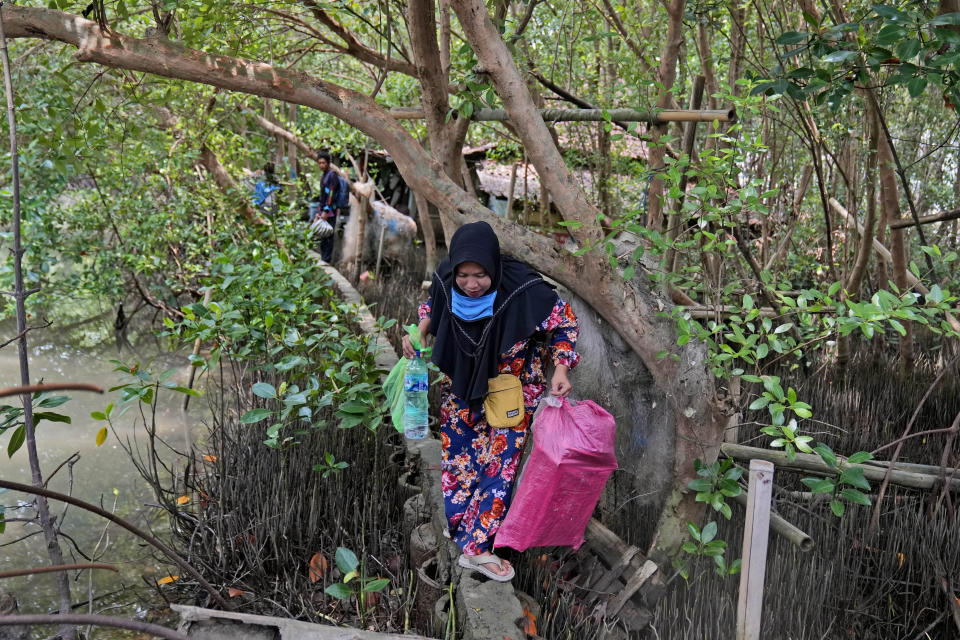 Asiyah navigates her steps on a narrow concrete slab, the only way to access her abandoned house, while carrying plastic bags containing items she recovered from her old house in Mondoliko, Central Java, Indonesia, Monday, Sept. 5, 2022. She and her family eventually moved to drier land, becoming climate migrants as many of their neighbors had before them. (AP Photo/Dita Alangkara)