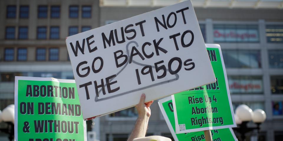 A hand holds a sign: "We must not go back to the 1950s"