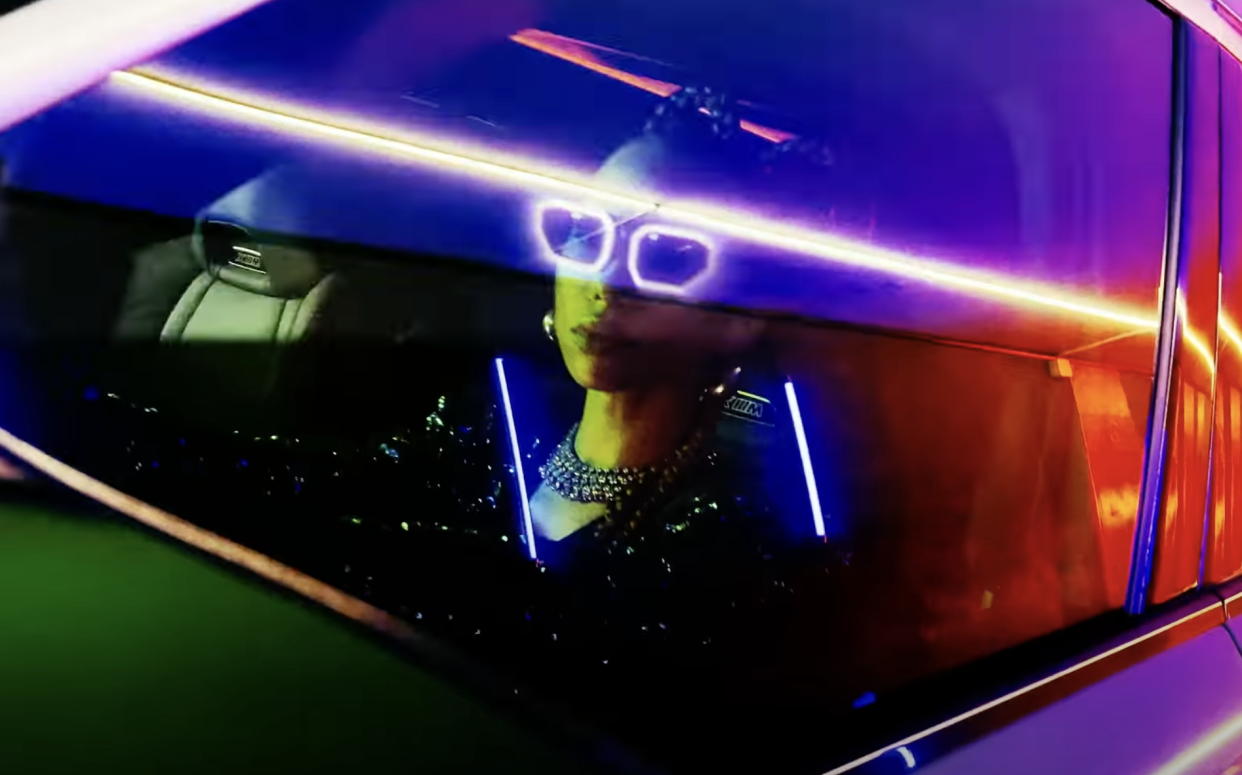 A person is shown driving the XM through windows with colorful reflections in this screenshot from the BMW XM release video.