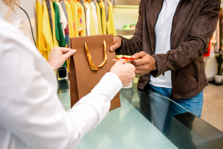 A sales clerk handing the customer their credit card and their items in a bag.