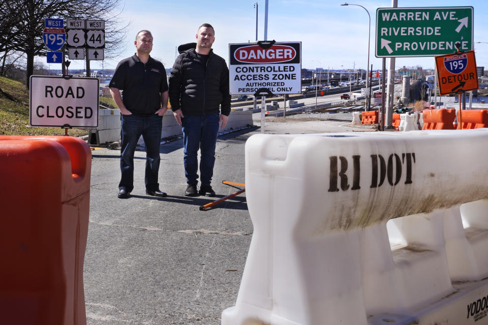 Marco Pacheco, left, owner of Jordan's Liquors and John Oliver, owner of The Local sports bar, pose at the closed onramp leading to the Washington Bridge, near their businesses, Friday, March 8, 2024, in East Providence, R.I. The closure of a section of the bridge, and onramps, due to failure of some bridge components, has caused a significant loss to local businesses. (AP Photo/Charles Krupa)
