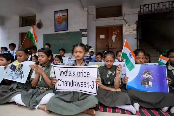 Young people sitting on a rug in a classroom hold flags and signs reading