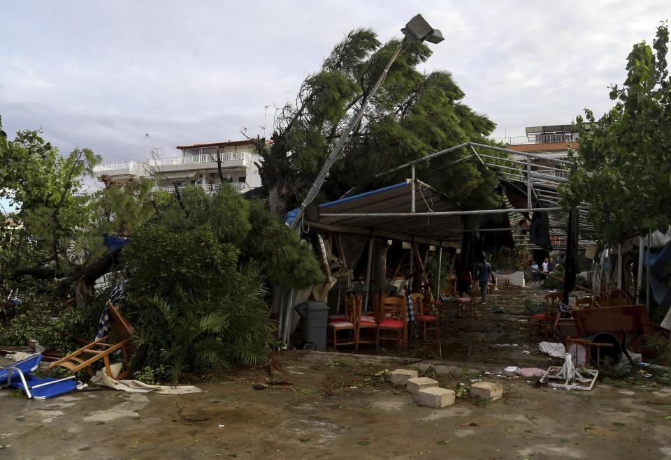 People look a damaged restaurant after a storm at Nea Plagia village in Halkidiki region, northern Greece on Thursday, July 11, 2019. A child and his mother died when they hit by the outdoor restaurant's lean-to roof that collapsed. A powerful storm hit the northern Halkidiki region late Wednesday. (Giannis Moisiadis/InTime News via AP)