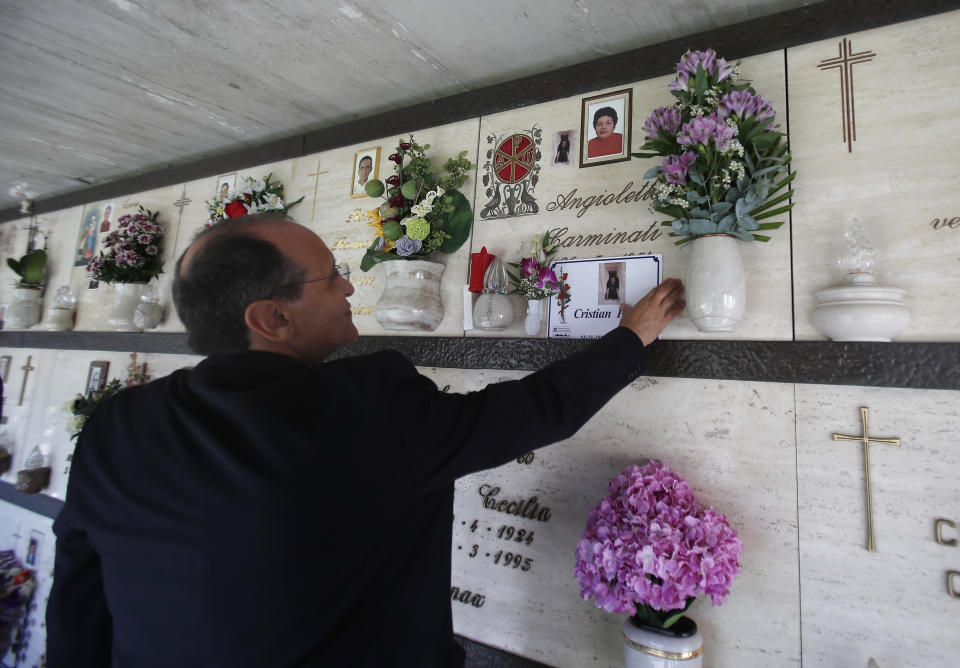 FILE - Priest Mario Carminati touches a picture of his nephew Christian Persico, who died from symptoms of coronavirus, at a cemetery in Casnigo, near Bergamo, Italy, Sunday, Sept. 27, 2020. "This thing should make us all reflect. The problem is that we think we're all immortal," the priest said. (AP Photo/Antonio Calanni)
