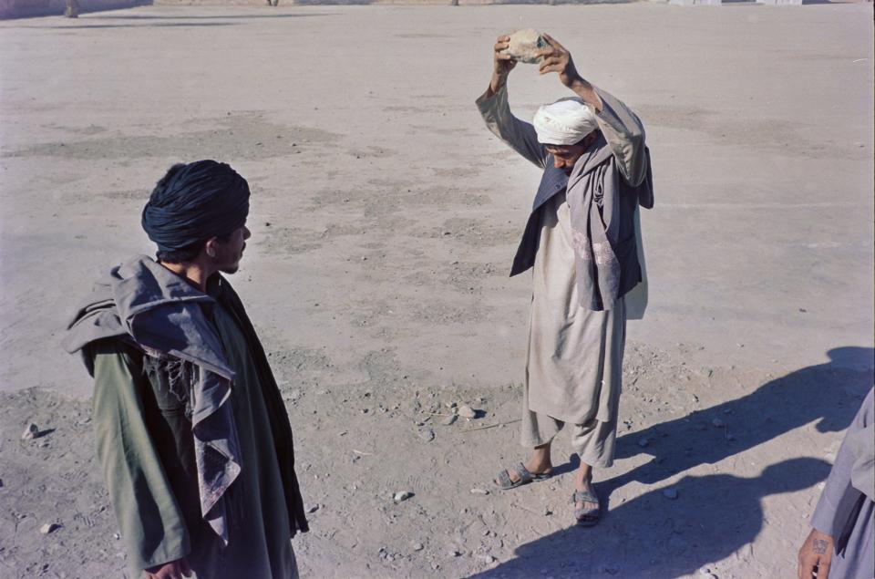 A man holds a stone high above his head as a second man looks on.