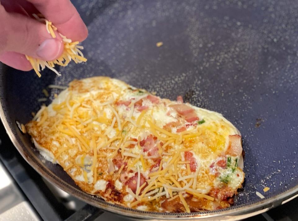 hand sprinkling cheese on a fried egg in a pan