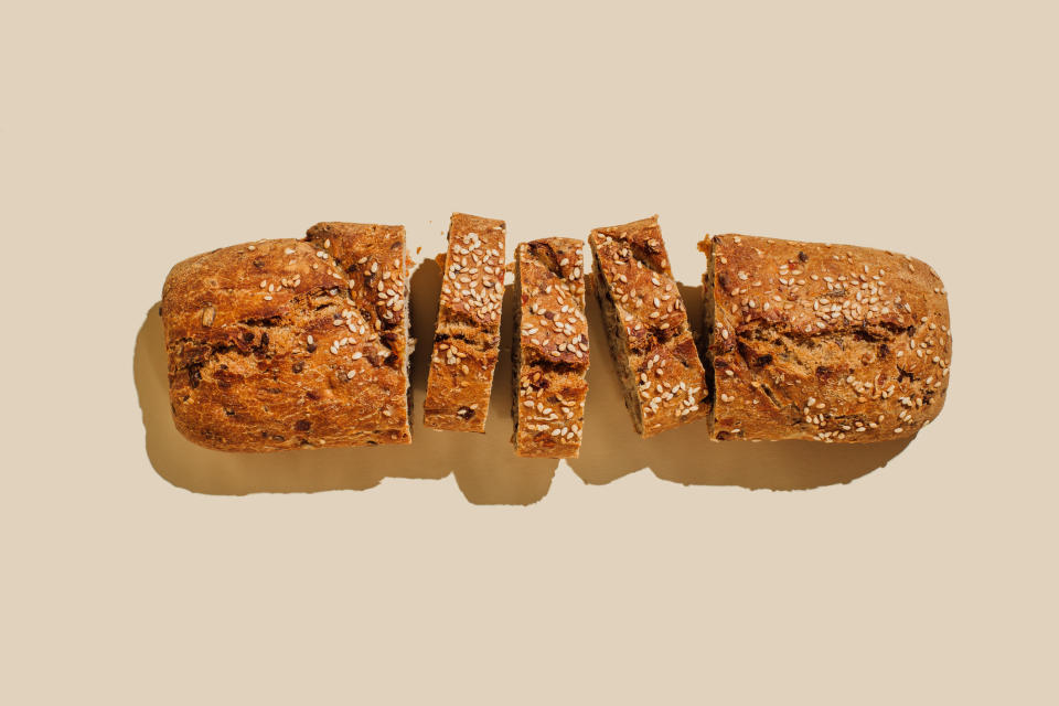 Sliced loaf of whole grain bread with mixed seeds on a plain background