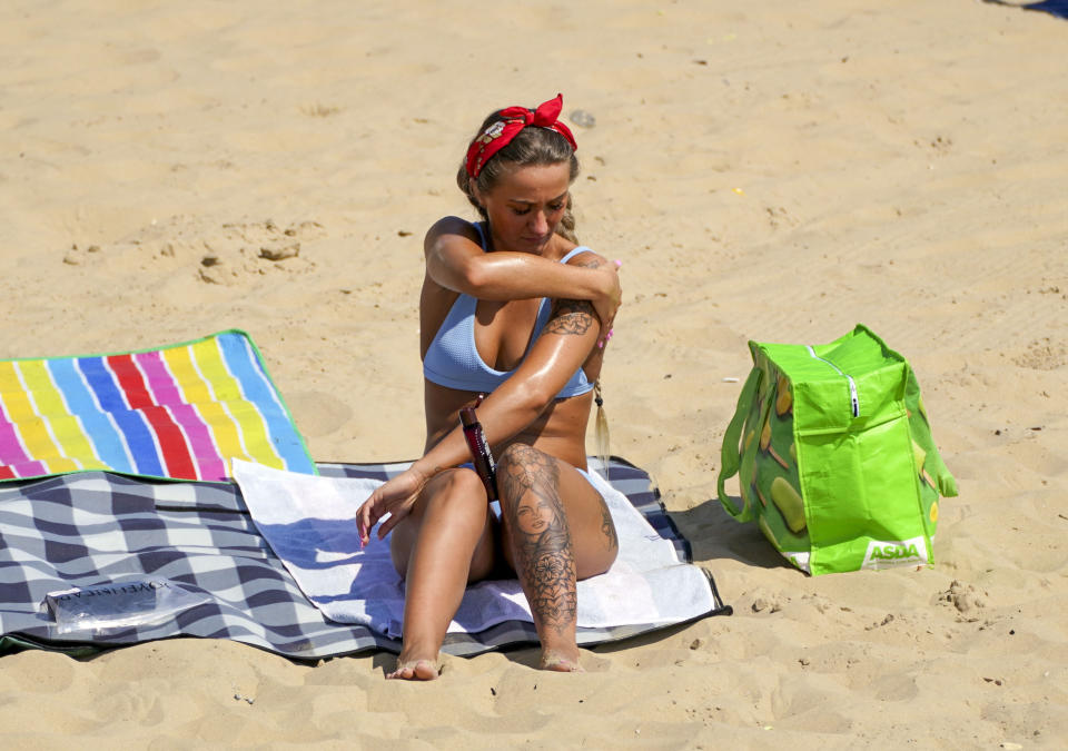 <p>A bather applies lotion as people enjoy the weather on Bournemouth beach in Dorset. Picture date: Monday July 19, 2021.</p>
