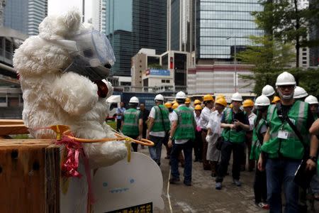 Workers from the Lands Department gather to remove encampments as a teddy bear wearing a mask is displayed by pro-democracy protesters outside the government headquarters in Hong Kong, China June 24, 2015. REUTERS/Bobby Yip