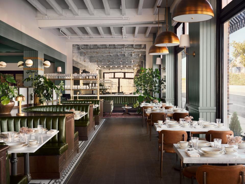 A restaurant with green booths, light green walls, big windows, and exposed white beams.