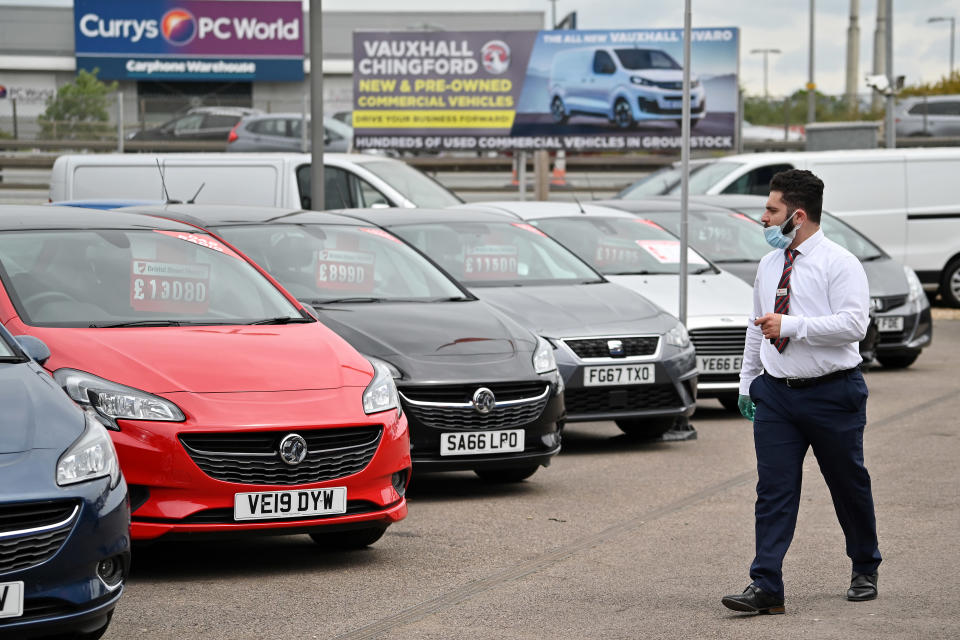 A car sales person wearing PPE (personal protective equipment) including a face mask and gloves as a precautionary measure against COVID-19, walks past vechiles parked on the forecourt of a recently re-opened Vauxhall car dealership in north London on June 4, 2020, as lockdown restrictions are eased during the noel coronavirus COVID-19 pandemic. - Car showrooms in England reopened this week as the UK government eased COVID-19 lockdown measures that have slammed the brakes on the industry. (Photo by JUSTIN TALLIS / AFP) (Photo by JUSTIN TALLIS/AFP via Getty Images)