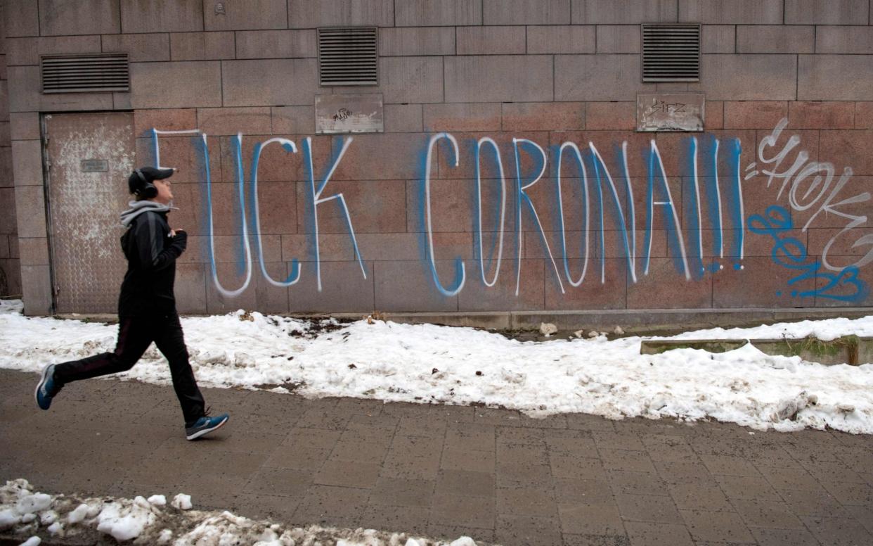 A jogger runs past graffiti reading "F*** Corona" in the Sodermalm neighbourhood of Stockholm - ANDERS WIKLUND /ANDERS WIKLUND 