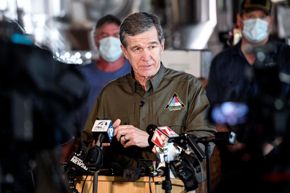North Carolina Governor Roy Cooper stands in front of a row of muddied volunteers as he speaks to the press at BearWaters Brewing in Canton August 19, 2021.