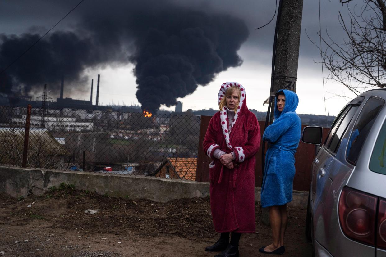 Women stand in their robes as smoke rises in the background after shelling in Odesa, Ukraine, Sunday, April 3, 2022. 