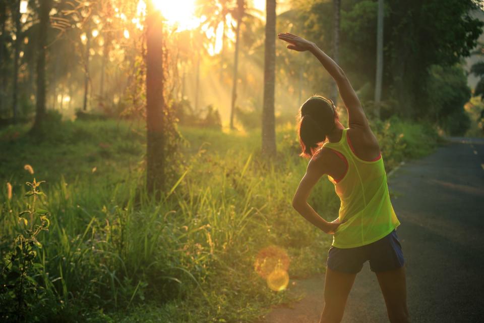 young female runner warming up before running at morning forest trail