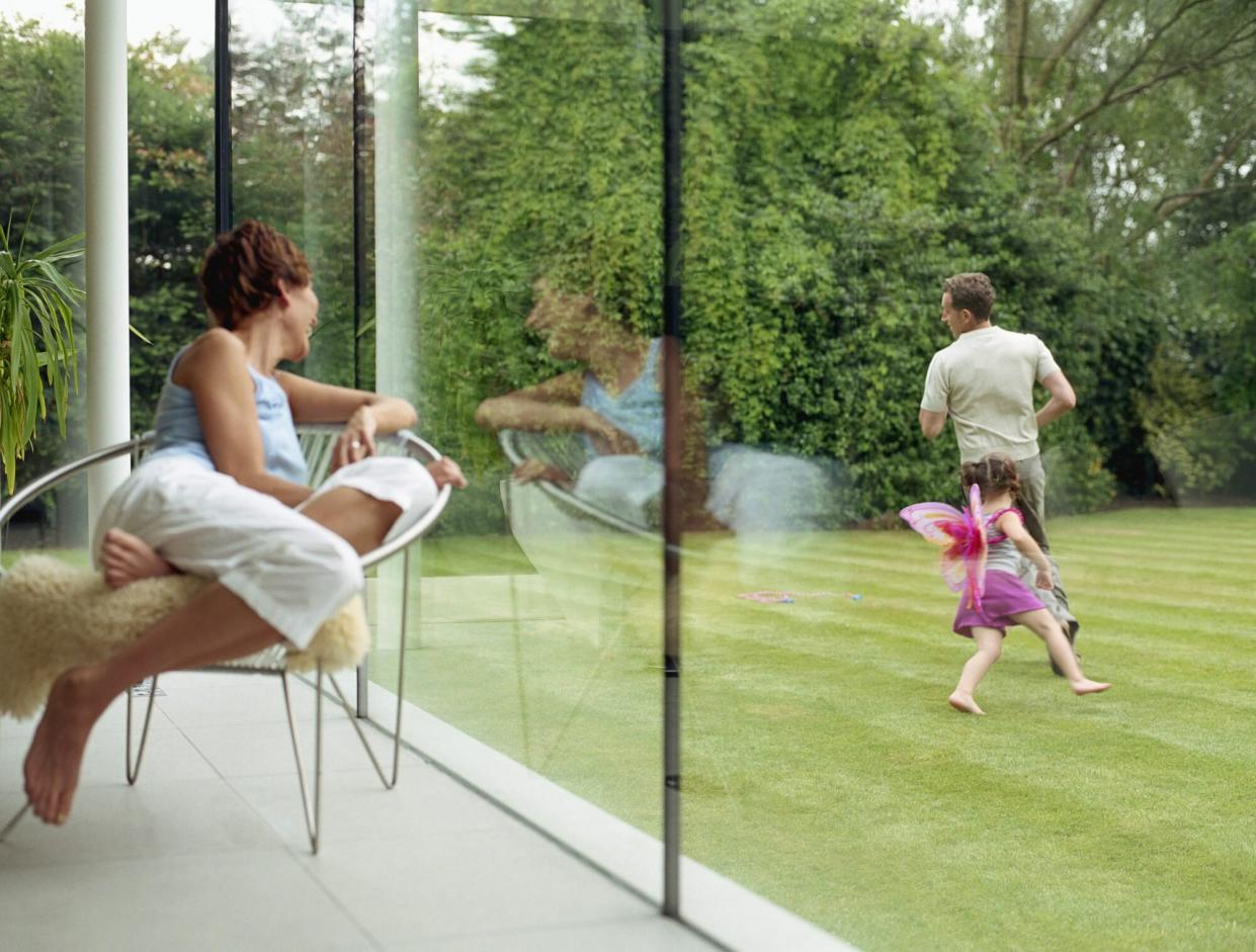 Woman looking out of window at father and daughter running in yard