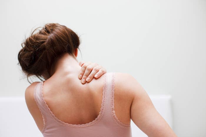 A person seen from behind with a hand on their shoulder, possibly indicating soreness or tension