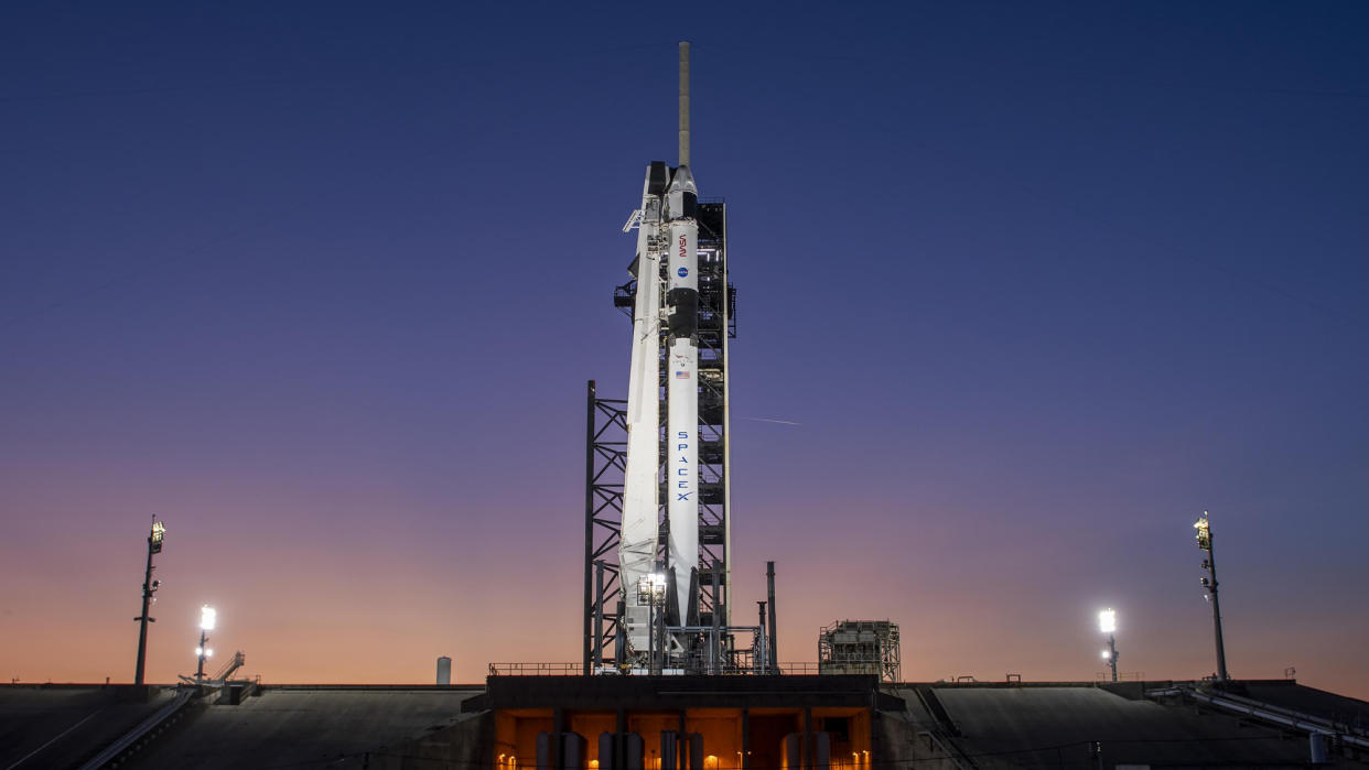  A black and white rocket stands on its launch pad with a purple twilight sky in the background. 
