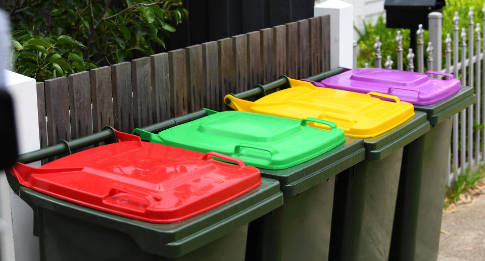 Four rubbish bins with red, green, yellow and purple lids.