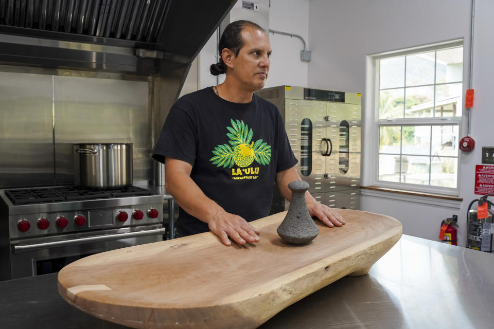 Hokuao Pellegrino touches a poi board he carved with a piece of breadfruit wood 20 years ago at Noho'ana Farm on Tuesday, Oct. 10, 2023, in Waikapu, Hawaii. (AP Photo/Mengshin Lin)