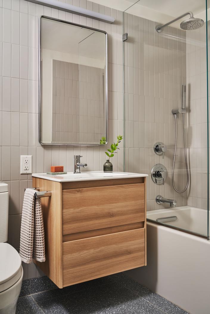 APRÈS : La salle de bains singulière de l'appartement a reçu un design intemporel et moderne de carreaux de métro installés verticalement.