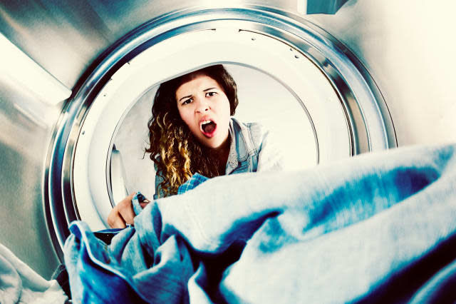 Horrified young woman grimaces at laundry in clothes drier