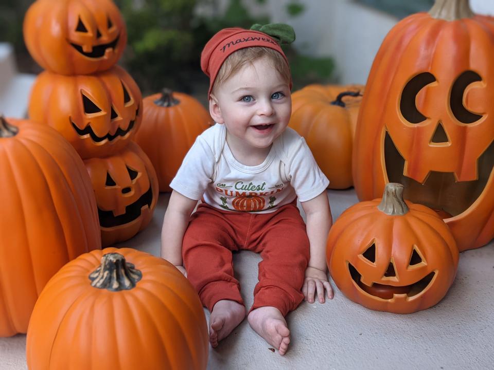 Helena McCabe's son, Max, wearing orange pants and a white shirt sitting with jack-o-lanterns