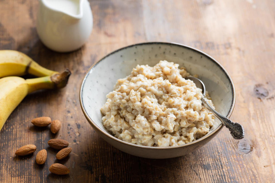 Oatmeal porridge in bowl served with banana, almonds and almond milk for healthy breakfast. Old wooden table background. Healthy lifestyle concept