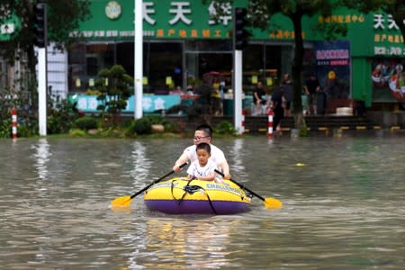Man rows an inflatable kayak carrying a boy on a flooded street after Typhoon Lekima hit Wenling, Zhejiang