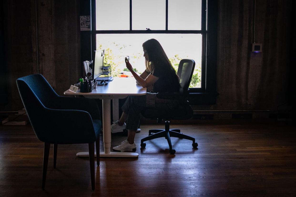 A woman talking on a cellphone while sitting at a desk in front of a window