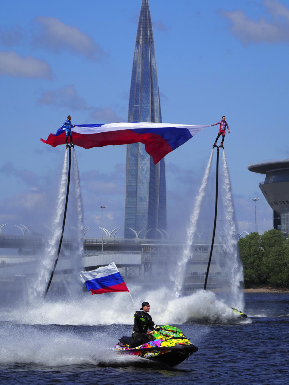 Members of the Russian hydroflight team hold the Russian national flag during the Day of Russia celebration in St.Petersburg, Russia, Friday, June 12, 2020, with business tower Lakhta Centre, the headquarters of Russian gas monopoly Gazprom in the background. (AP Photo/Dmitri Lovetsky)