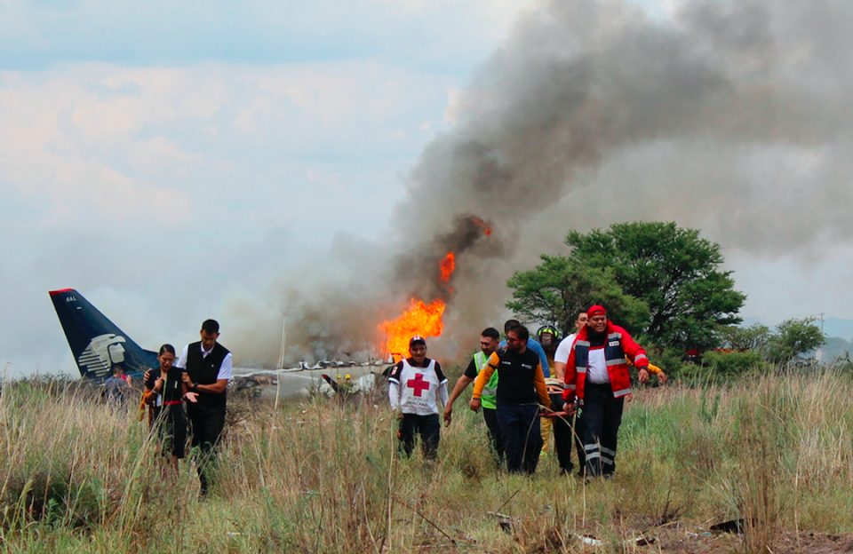 <em>Red Cross workers and rescue workers carry an injured person on a stretcher as airline workers walk away from the crash site (AP)</em>