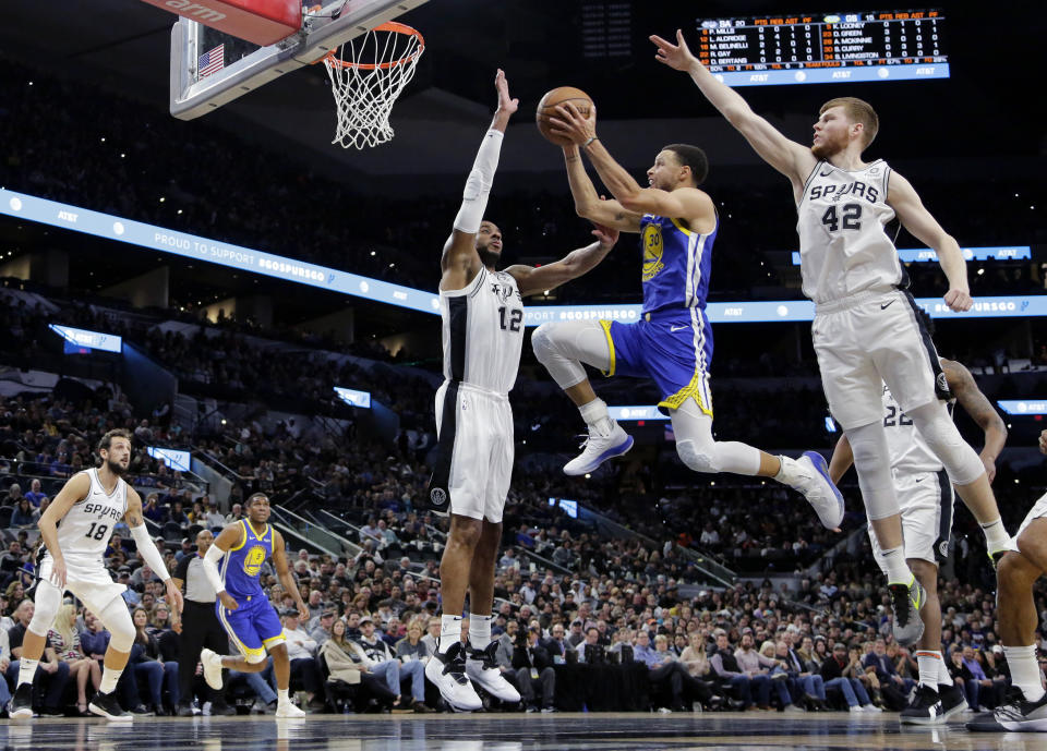 Golden State Warriors guard Stephen Curry (30) drives to the basket against San Antonio Spurs center LaMarcus Aldridge (12) and forward Davis Bertans (42) during the first half of an NBA basketball game, in San Antonio, Monday, March 18, 2019. (AP Photo/Eric Gay)