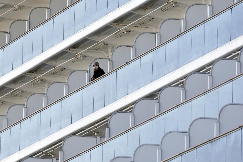A passenger stand outside on the balcony of the cruise ship Diamond Princess anchored at the Yokohama Port Thursday, Feb. 6, 2020, in Yokohama, near Tokyo. The 3,700 people on board faced a two-week quarantine in their cabins. Health workers said 10 more people from the Diamond Princess were confirmed sickened with the virus, in addition to 10 others who tested positive on Wednesday. The 10 will be dropped off as the ship docks and transferred to nearby hospitals for further test and treatment. (AP Photo/Eugene Hoshiko)
