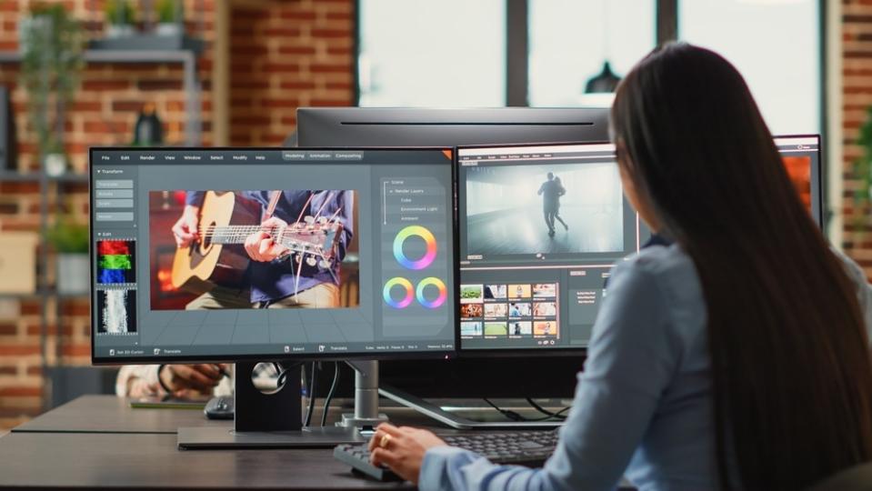 A woman looks at computer screens showing image editing software.