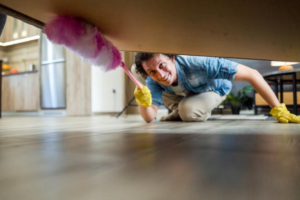 Man cleaning cobwebs under bed