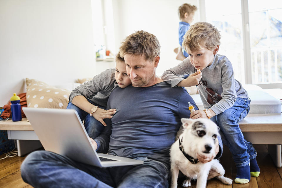 Father using laptop at home with children watching