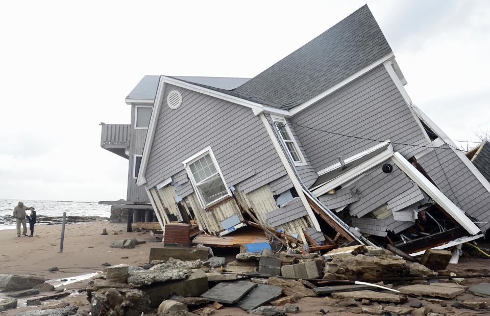 FILE - In this Tuesday, Oct. 30, 2012 file photo, people stand next to a house collapsed from Superstorm Sandy in East Haven, Conn. While Connecticut was spared the destruction seen in New York and New Jersey, many communities along the shoreline, including some of the wealthiest towns in America, were struggling with one of the most severe storms in generations. (AP Photo/Jessica Hill, File)